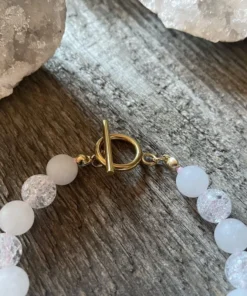 Náramok na americké zapínanie z krištáľu a ocele Gold. mliečne guľaté korálky a vnútri popraskané priesvitné korálky. v strede zlatý vysiaci štvorlístok. ukážka zapínania