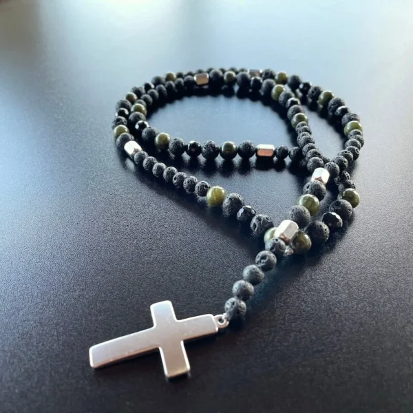 Luxusný pánsky náhrdelník Ónyx a Jadeit. Dlhý náhrdelník v tvare ruženca. Dĺžka pod hrudnú kosť. Čierne lesklé brúsené korálky, matné korálky lávového kameňa s malými prasklinkami. korálky jadeitu v lesklej tmavozelenej farbe. medzi korálkymi z polodrahokamov je šesť koráliek z nehrdzavejúcej ocele v tvare malých podlhovastýchkvádrov .visiaci štvor centimetrový nie veľmi lesklý oceľový kríž